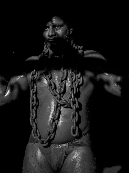 A series of dramatic, low-key portraits of a wrestler with heavy chains draped around his neck. These photos symbolize the immense strength and burden of the Pailwan's discipline.