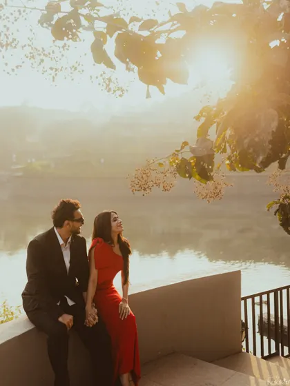 A romantic portrait of the couple sitting by a lake at sunrise, with the golden light filtering through the trees.