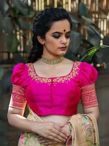 The intricate gold embroidery on this pink blouse is complemented by a classic gold choker, creating a rich and festive look.