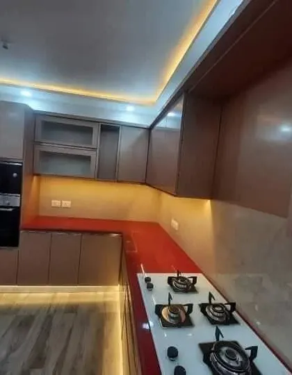 A beautiful modular kitchen with a striking red countertop and brown cabinets. The design includes a built in oven and microwave tower.