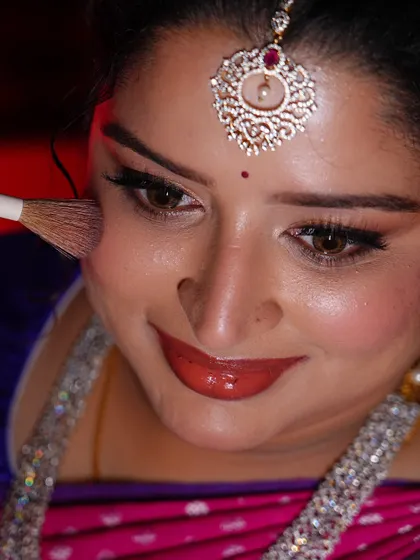 A close-up getting-ready shot. Applying blush to add a warm, rosy glow to the bride's cheeks for her engagement.