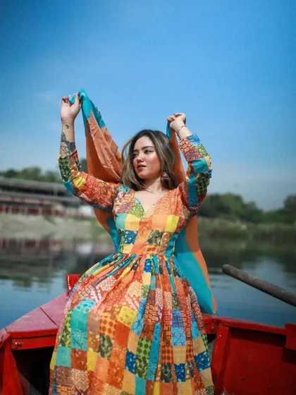 An ethnic wear shoot on a boat at Yamuna Ghat. The model's colorful patchwork dress contrasts beautifully with the blue sky and water.