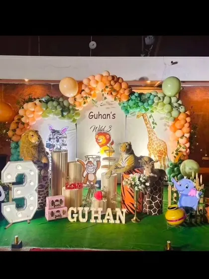 We created a complete jungle safari for Guhan's third birthday. The decor includes large animal props like a lion, tiger, and giraffe, along with a balloon arch in earthy tones and a personalized "Wild 3" backdrop.