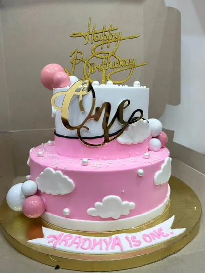 A lovely two-tiered cake for a first birthday. The pink and white design with clouds and spheres is a sweet and modern choice for a baby girl.