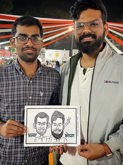 Two friends with their caricature at a lively outdoor event in Mumbai.