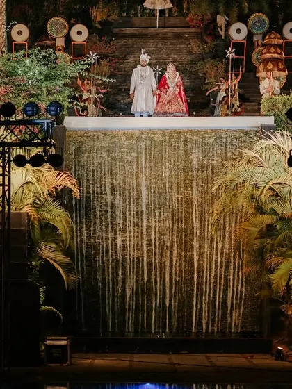 A wide-angle view of the Varmala stage set against a cascading waterfall. This highlights our ability to integrate natural or venue features into our event design for a unique and stunning effect.