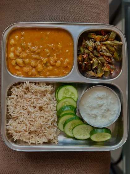 This balanced thali contains brown rice, channa masala, sautéed okra, fresh cucumber, and a side of curd for digestive health.