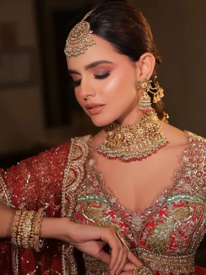 The intricate details of the gold jewelry set against the rich red of the lehenga. A timeless combination for any bride.