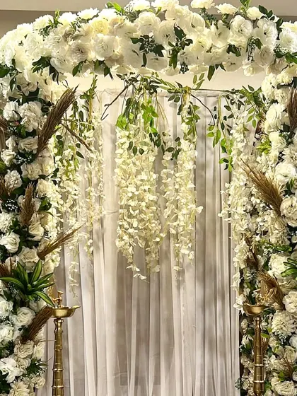 A modern and sophisticated Ganpati decor, this design blends elegant white flowers with trendy dried pampas grass and palm leaves.