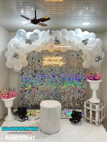 A glamorous silver-themed birthday setup. The iridescent shimmer wall is framed by a white and silver balloon arch, creating a dazzling effect.