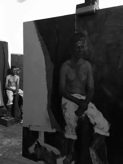 An in-process shot of a monochrome oil painting, with the live model sitting in the background.