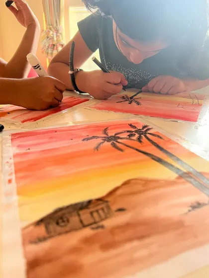 Adding the final touches. After painting the watercolor background, the kids use black markers to draw silhouettes, learning about foreground and background.