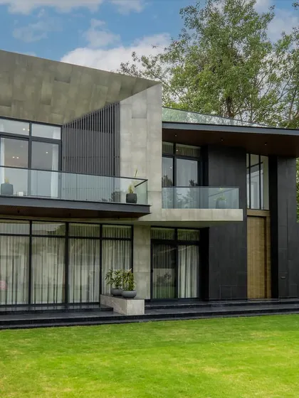 A closer look at the farmhouse project, highlighting the interplay between solid concrete volumes and dark, textured panels. The design emphasizes clean lines, cantilevered balconies, and a strong connection to the green landscape.
