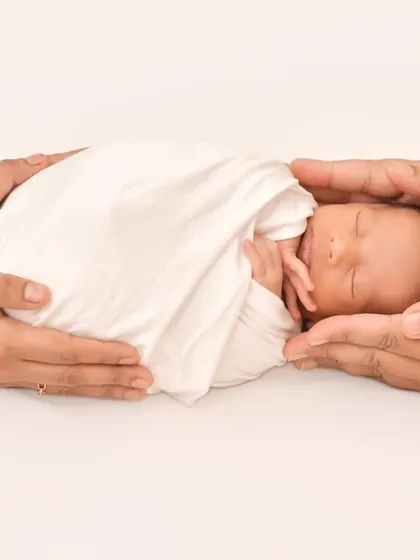 A delicate and symbolic photo of a sleeping newborn held safely and securely in the hands of their parents, highlighting how precious and small new life is.