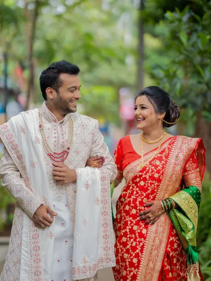 A candid walking shot of a happy Maharashtrian couple, capturing their genuine smiles and the elegance of their red and white wedding attire.