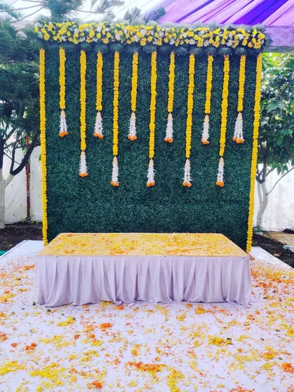 This outdoor haldi setup uses a similar green turf and marigold garland design, perfect for a daytime event. The scattered petals on the ground add an extra layer of color and festivity to the space.