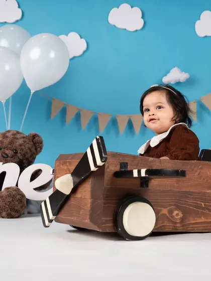 This little aviator girl is ready for takeoff in her wooden plane. The brown dress and sky-blue background create a lovely vintage feel.