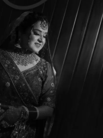 A classic black and white bridal portrait. The bride is looking down with a gentle smile, and the side lighting creates a soft, timeless feel that emphasizes her traditional attire.