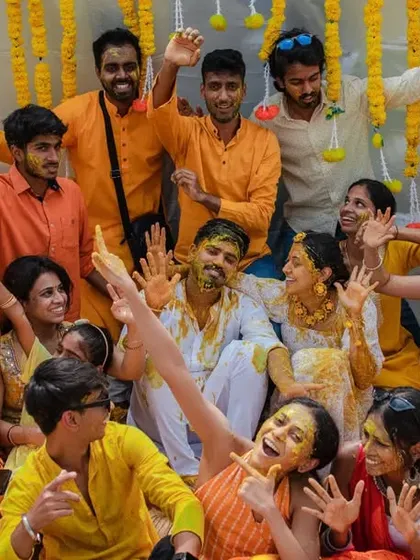 A fun and energetic group photo from a Haldi ceremony, with everyone waving and smiling. We capture the party atmosphere of your pre-wedding events.