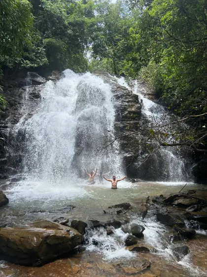 Another shot of trekkers with their arms outstretched, embracing the full force and beauty of the waterfall. It's a feeling of complete freedom.