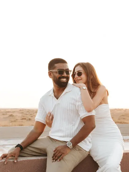 A relaxed and happy portrait of the couple enjoying the sunset. Their coordinated white outfits and genuine smiles make for a timeless and elegant pre-wedding picture.