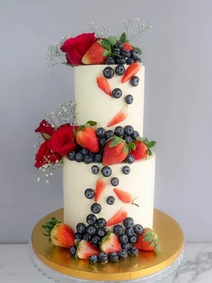 A beautiful two-tiered cake featuring a cascade of fresh strawberries and blueberries.