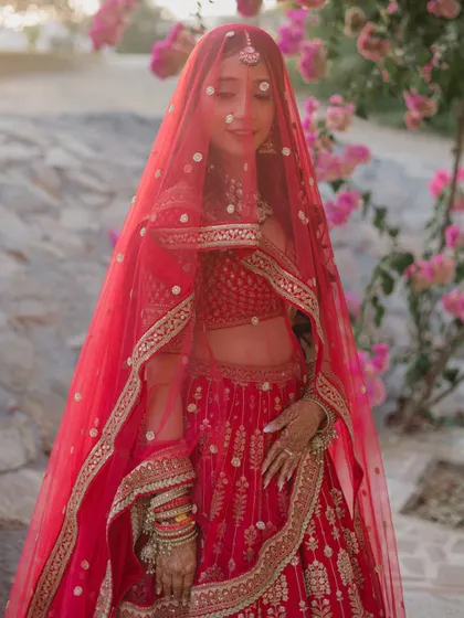 A classic bridal portrait, with the bride looking coyly through her red veil, surrounded by vibrant pink bougainvillea.