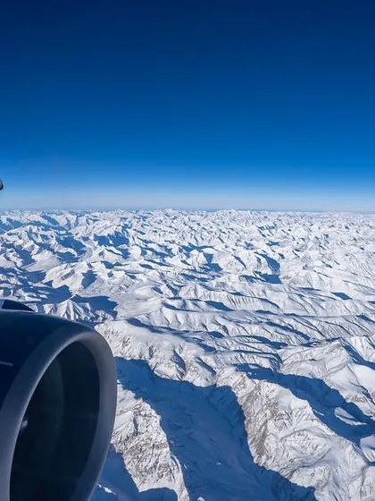 The snow-covered Himalayas as seen from a window seat on a flight to Leh. This aerial perspective reveals the vast, rugged, and beautiful high-altitude desert of Ladakh in winter.