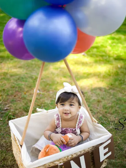 A gentle, curious look from the birthday girl. The colorful balloons add a festive touch to this lovely outdoor portrait.