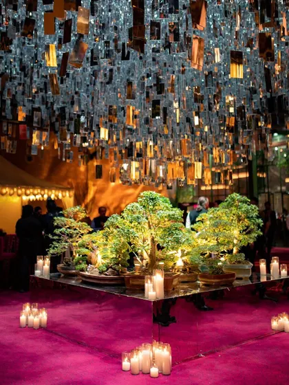 A modern and chic Sangeet setup featuring a ceiling of hanging mirrored tiles over a central display of bonsai trees.