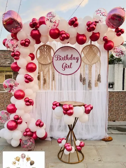 A beautiful rooftop boho-chic photo booth with a white curtain, macrame dreamcatchers, and a pink and white balloon arch.
