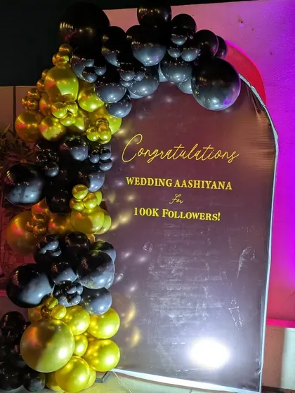 A clean, well-lit shot of a custom backdrop for a corporate client celebrating a social media milestone. The balloon garland adds a three-dimensional, festive element to the branded message.