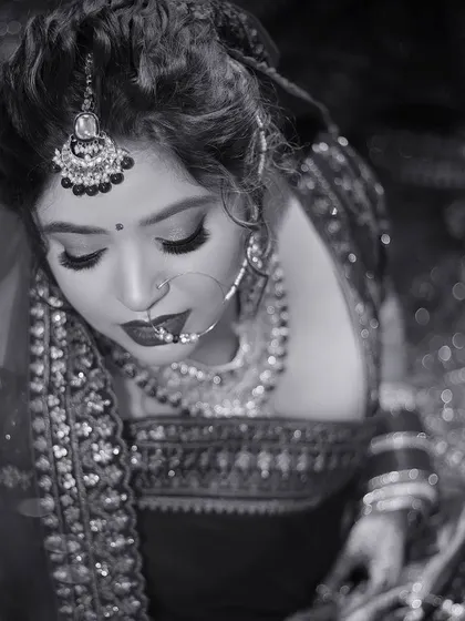 A classic black and white portrait of the bride, looking down with a serene expression. The focus is on her intricate jewelry and makeup.
