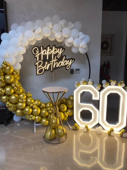 A classic and clean setup for a 60th birthday, featuring a half-arch of white balloons and a base of gold balloons.