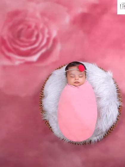 A simple and elegant shot of a baby in a pink swaddle, resting in a basket against a soft-focus pink rose background.