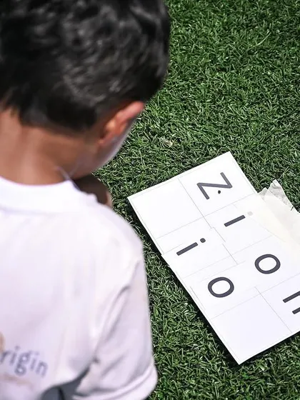 A student works on a name-spelling puzzle as part of a sports day activity, combining literacy with physical challenges.