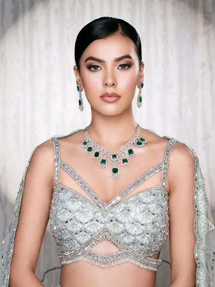 A clean and polished mid-shot against a textured background, allowing the details of the mint green blouse and emerald jewelry to shine.