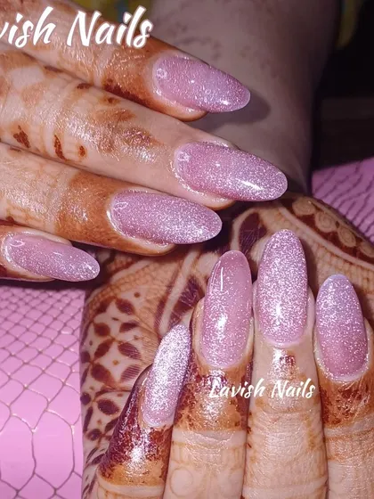 A full set of almond-shaped extensions with a sparkling pink glitter finish, shown against a hand with fresh mehendi to highlight how the shimmer complements the art.