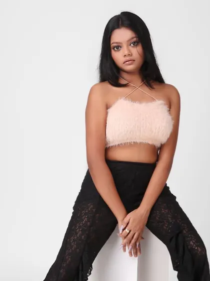 This three-quarter shot captures a model in a trendy outfit, featuring a pink fur crop top and black lace pants. The simple white background ensures the focus remains on the fashion look.