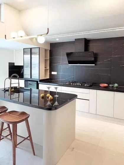 A luxurious kitchen design featuring a large island with bar seating, a striking black marble backsplash, and dual-toned cabinetry. The modern pendant light adds a final touch of sophistication.