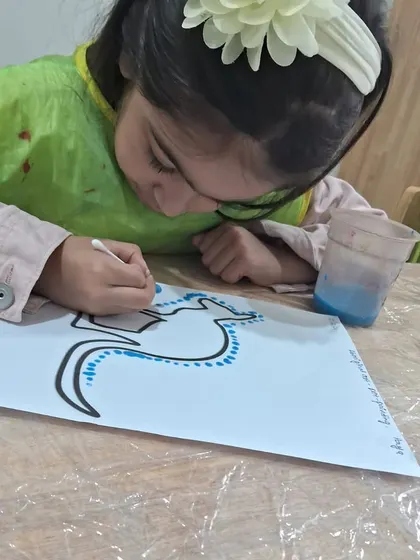 With a flower in her hair, this girl leans in close to her artwork. The concentration on her face shows how engaging this cultural art activity is.