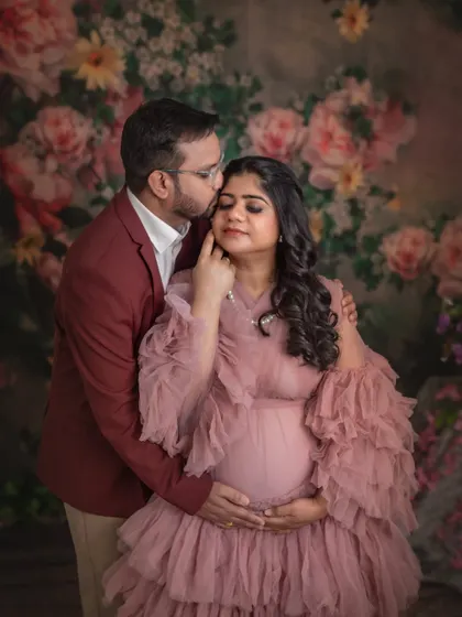A husband gently kisses his wife's forehead as they embrace during their maternity shoot. The floral background and their tender expressions create a deeply romantic and emotional photograph.