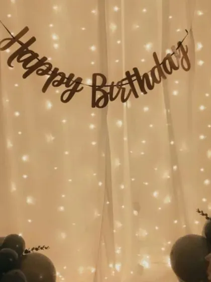 A simple and elegant backdrop created with a curtain of fairy lights. A "Happy Birthday" banner is hung across the top, creating a warm and inviting atmosphere for a home celebration.