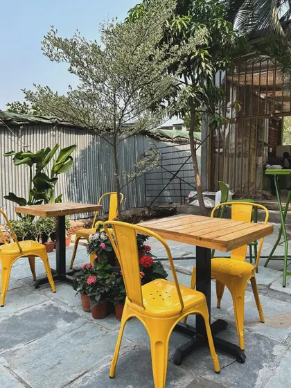A sunny day in our outdoor seating area. The combination of natural wood tables, colorful chairs, and surrounding trees makes it a perfect spot for a bright and airy lunch.
