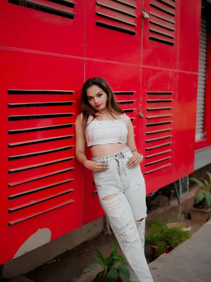 A full-length portrait against a vibrant red wall. The model's relaxed pose and casual outfit make this a great example of modern street style.