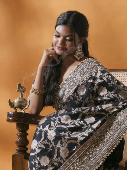 This portrait captures a moment of quiet reflection, blending traditional elegance with a contemporary mood. The intricate details of the black and gold saree are highlighted by soft, directional lighting, creating an image that is both artistic and deeply personal.