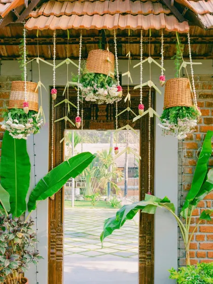 The entrance to the Muhurtham ceremony, decorated with hanging wicker baskets filled with flowers and traditional thoran, framed by auspicious banana plants.