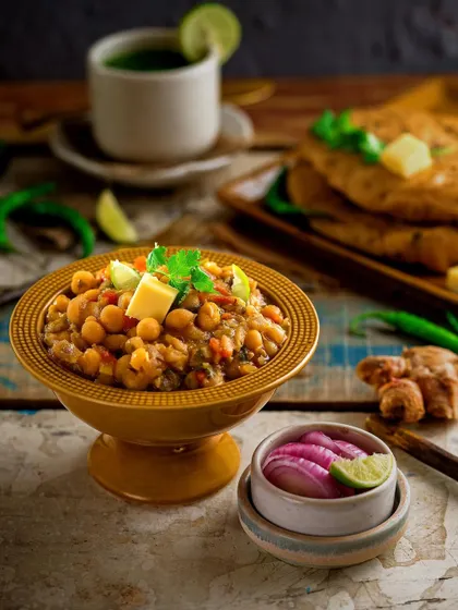 A classic North Indian meal of Chole Kulche, styled with fresh ingredients. The fluffy kulche and rich chickpea curry are presented with pickled onions and ginger, creating a mouth-watering image of this popular street food.