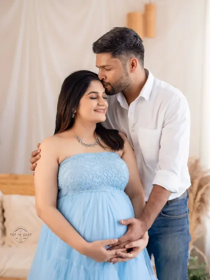 An intimate couple's portrait capturing a sweet forehead kiss. The mom-to-be wears a lovely light blue tulle gown, perfect for our boho-chic studio setup.