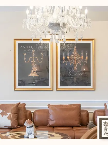 These Victorian-style wall art pieces, featuring antique lighting fixtures, add a layer of classic charm. The gold frames and dark background create a dramatic and luxurious look above the brown leather sofa.